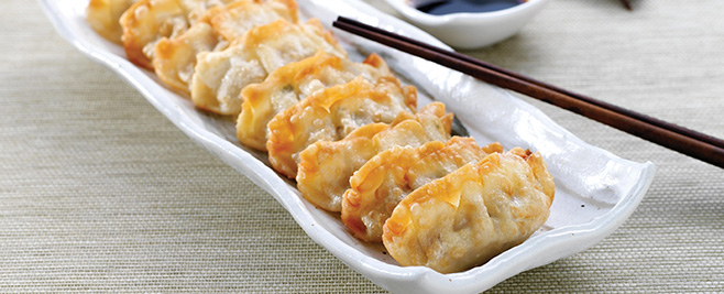 several potstickers in a white dish with black chopsticks